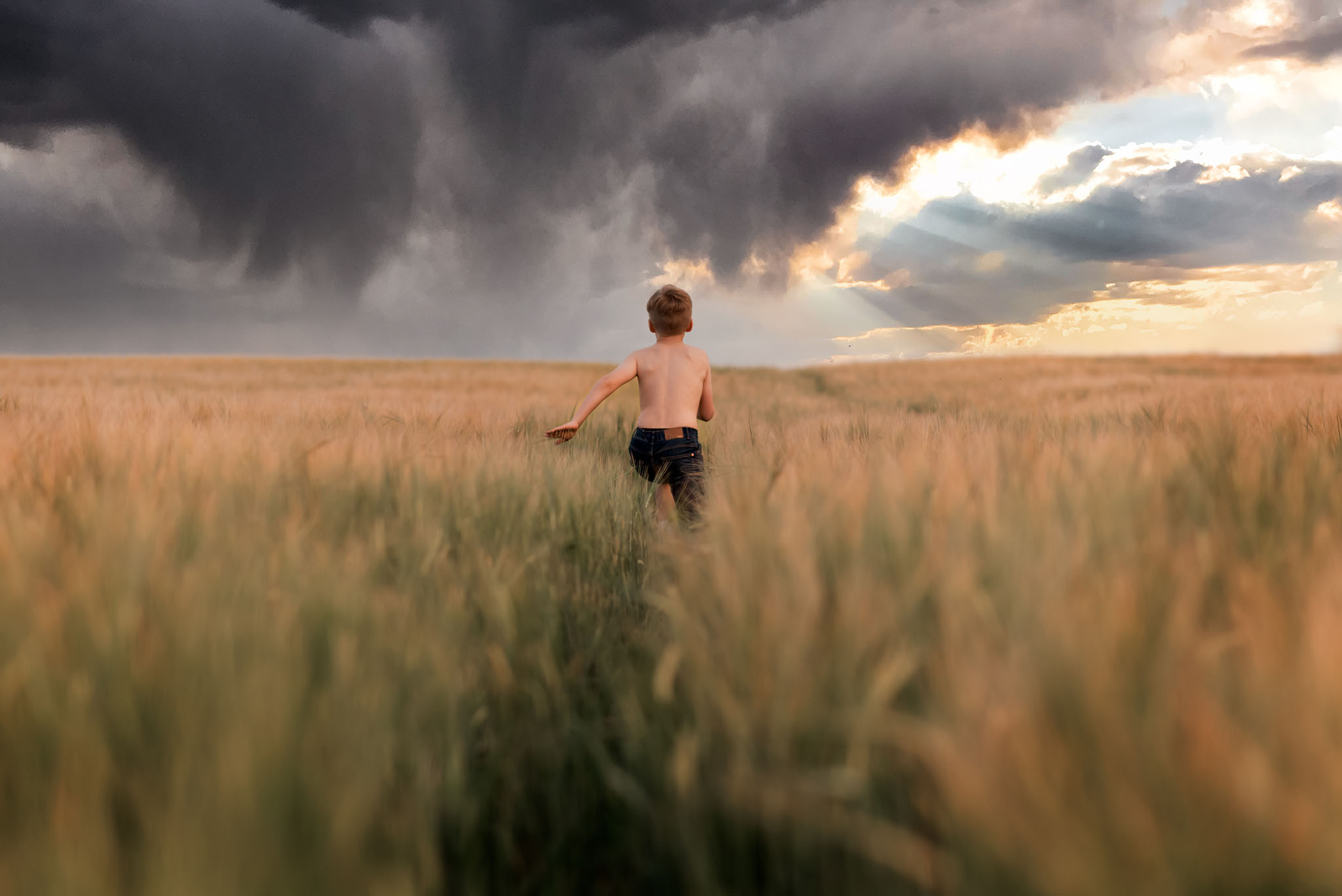 Child running through a field with stormy sky