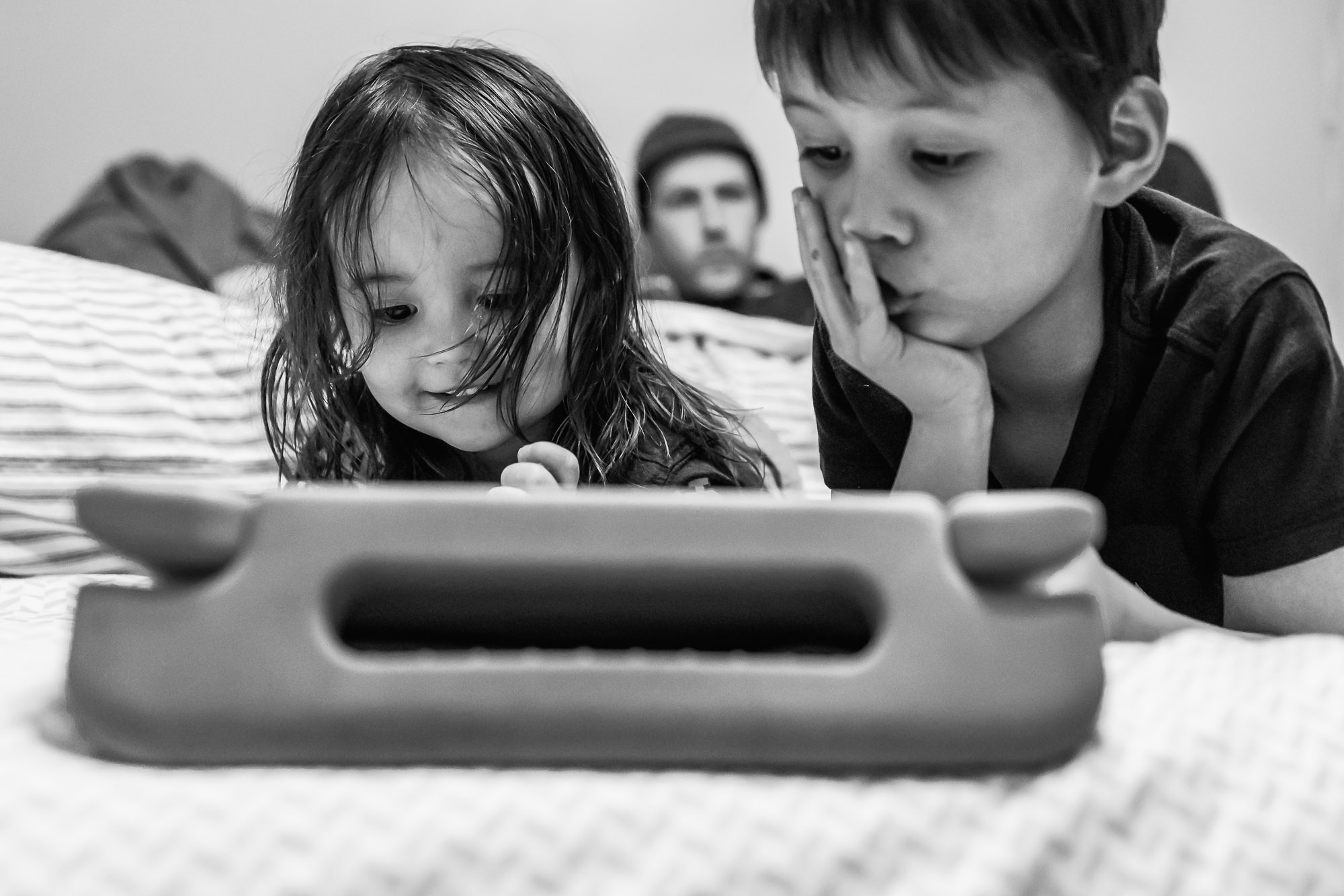Children playing on tablet with dad in background