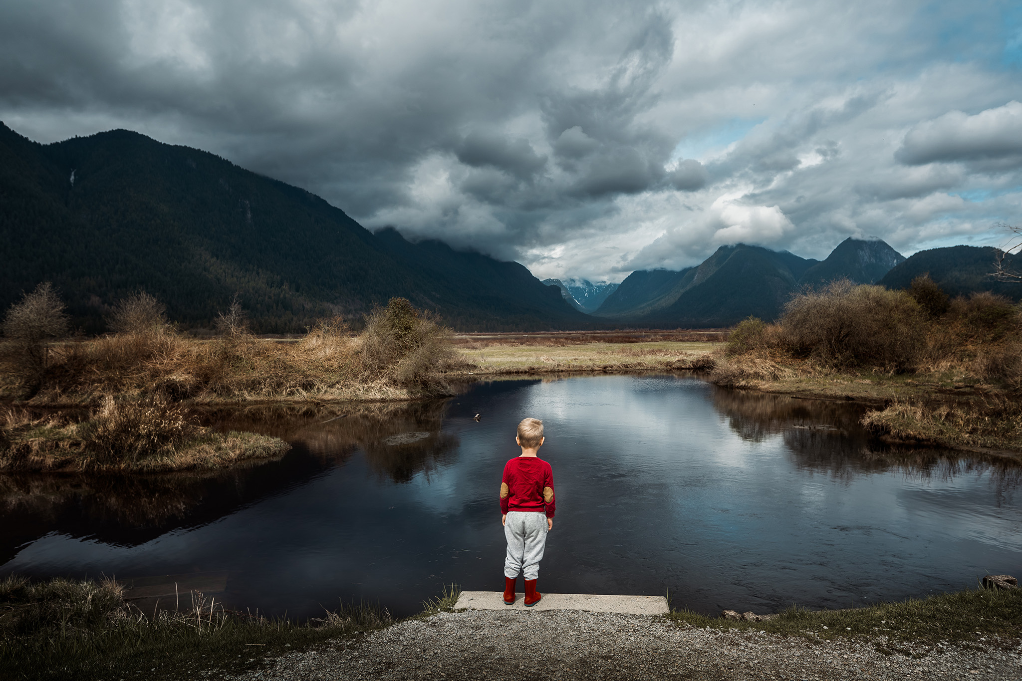 Child in red looking at the mountains in front of lake